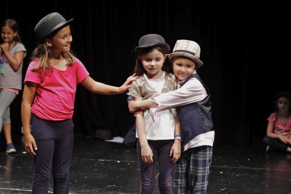 Group of kids acting on stage, wearing hats, showing empathy