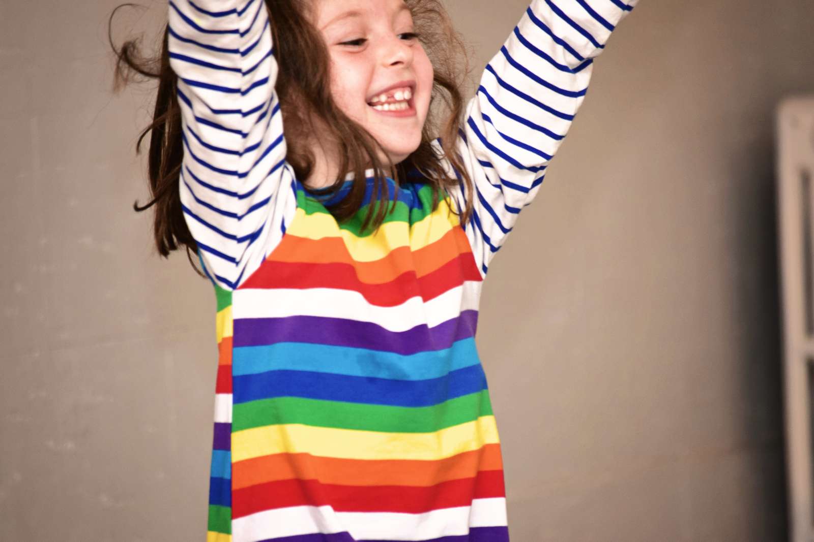 Girl in rainbow striped shirt smiling with arms up in the air